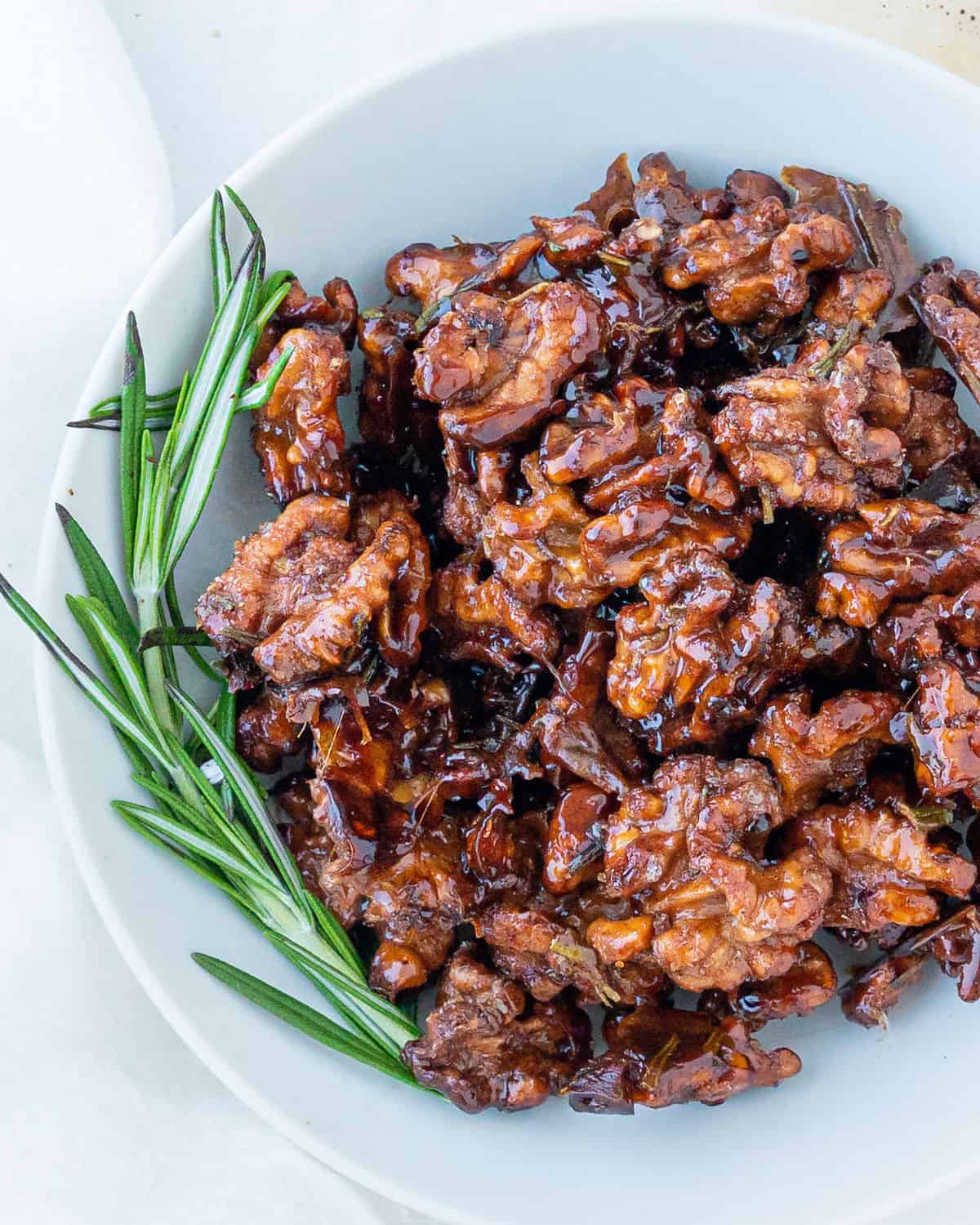 completed sweet rosemary walnuts plated on a white plate against a white surface