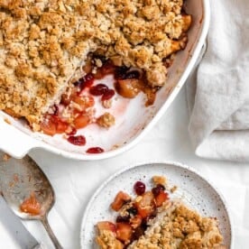 completed Apple Cranberry Crisp with a piece plated on a small white pplate against a white background