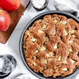 finished apple cake with two apples and measuring tools against a white background