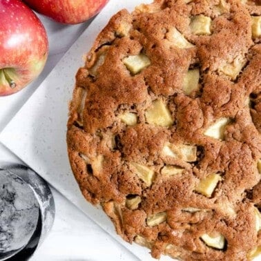 finished apple cake with two apples and measuring tools against a white background