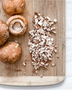 finely diced mushrooms on a brown cutting board with whole mushrooms on the side