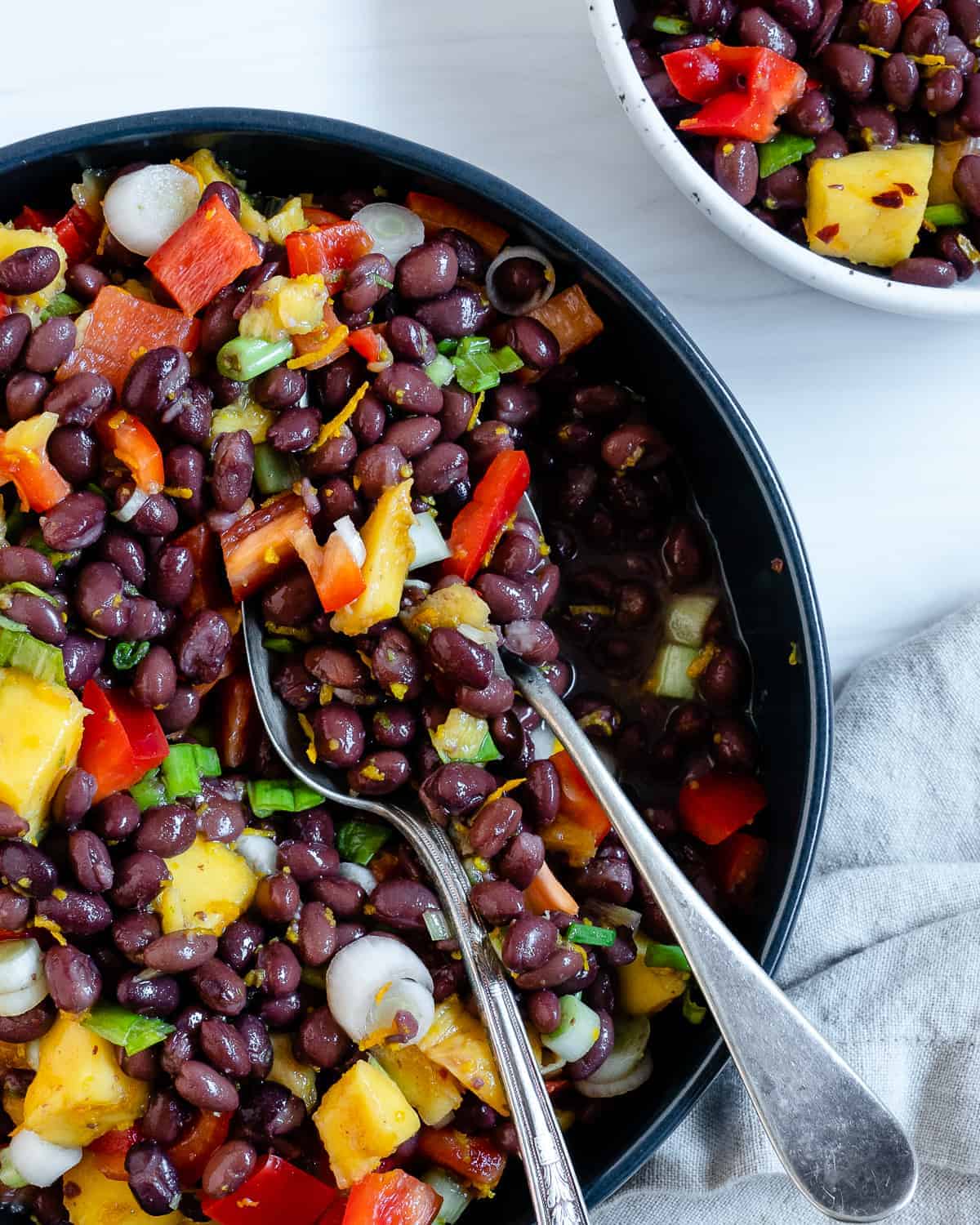 completed mango bean salad in a dark bowl with utensils in the bowl against a white background