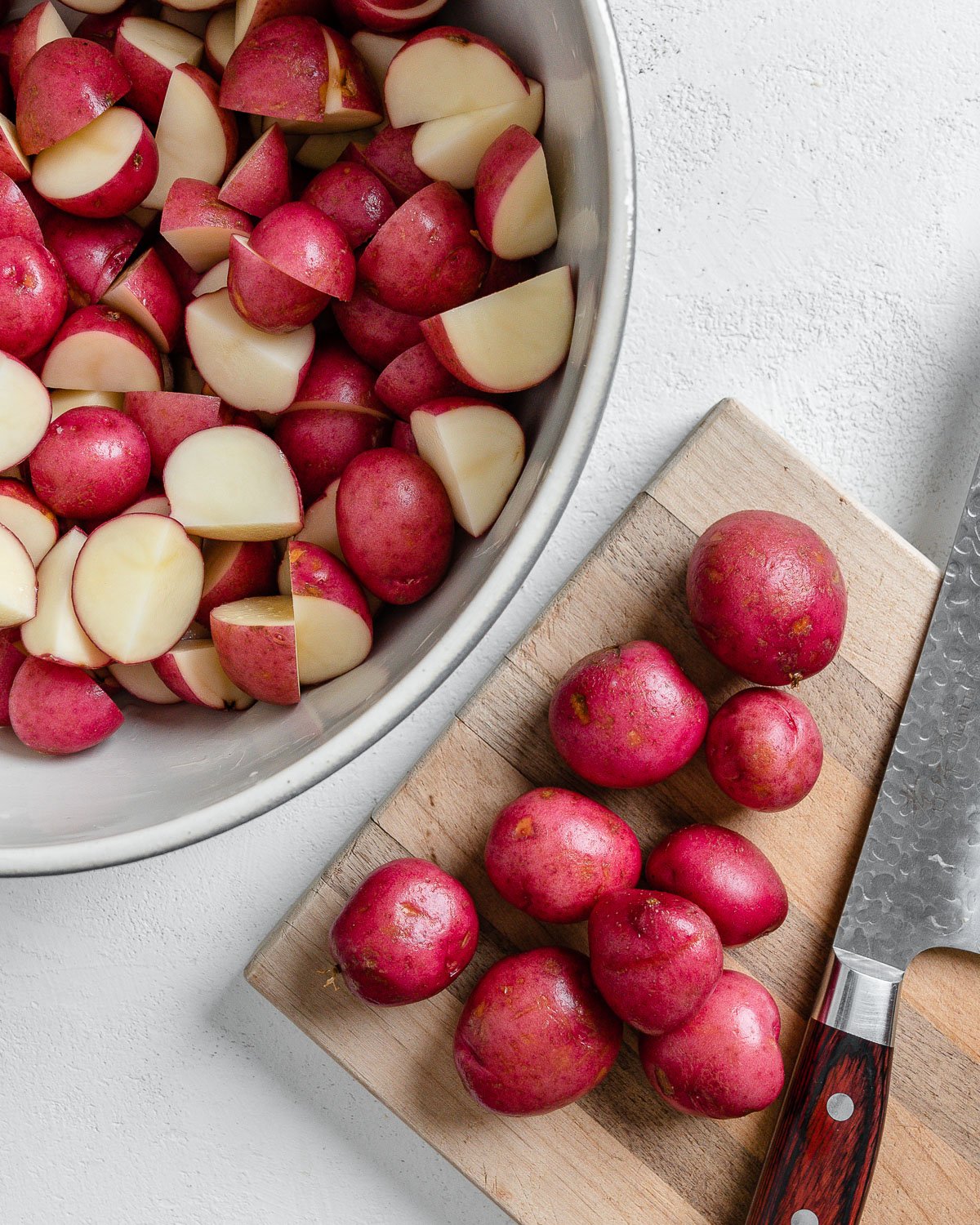 process of cutting potatoes with cut potatoes in a bowl and whole potatoes on a brown cutting board