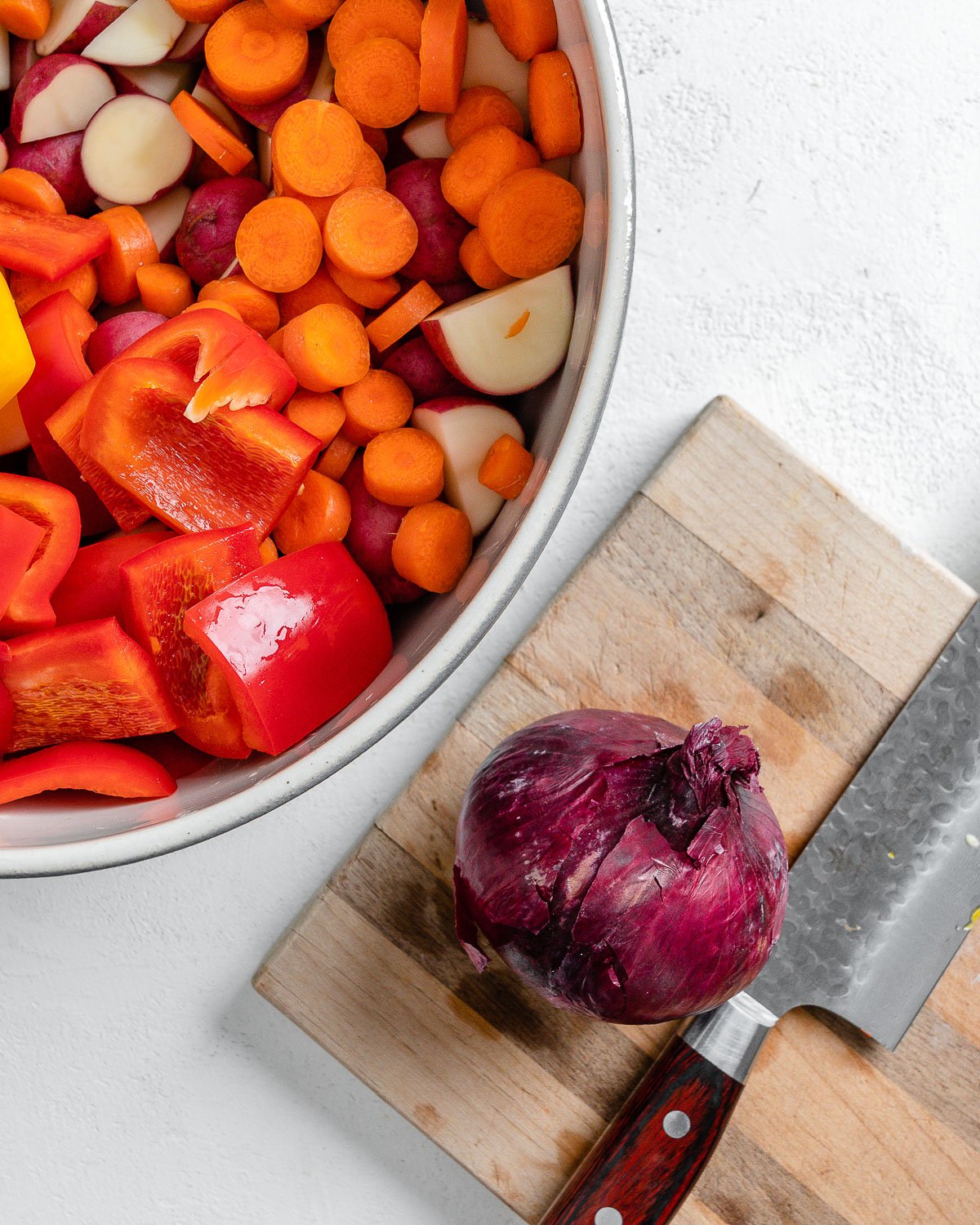 whole onion on cutting board alongside bowl of veggies