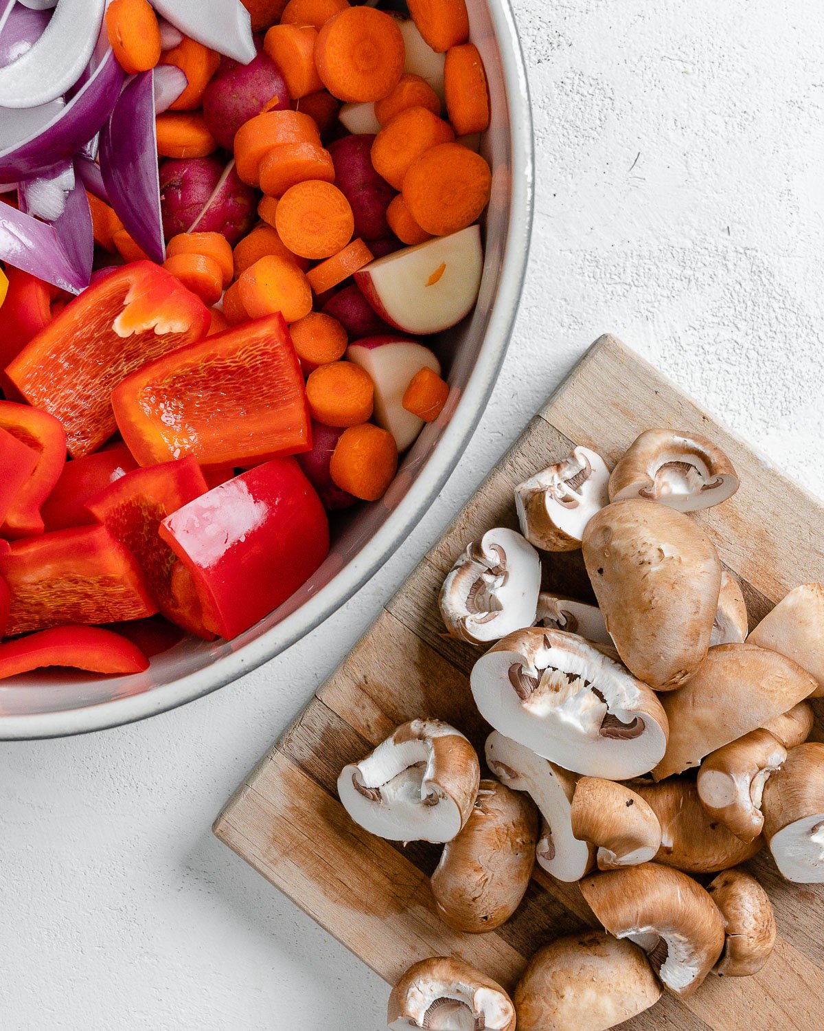 chopped mushrooms on cutting board alongside bowl of veggies