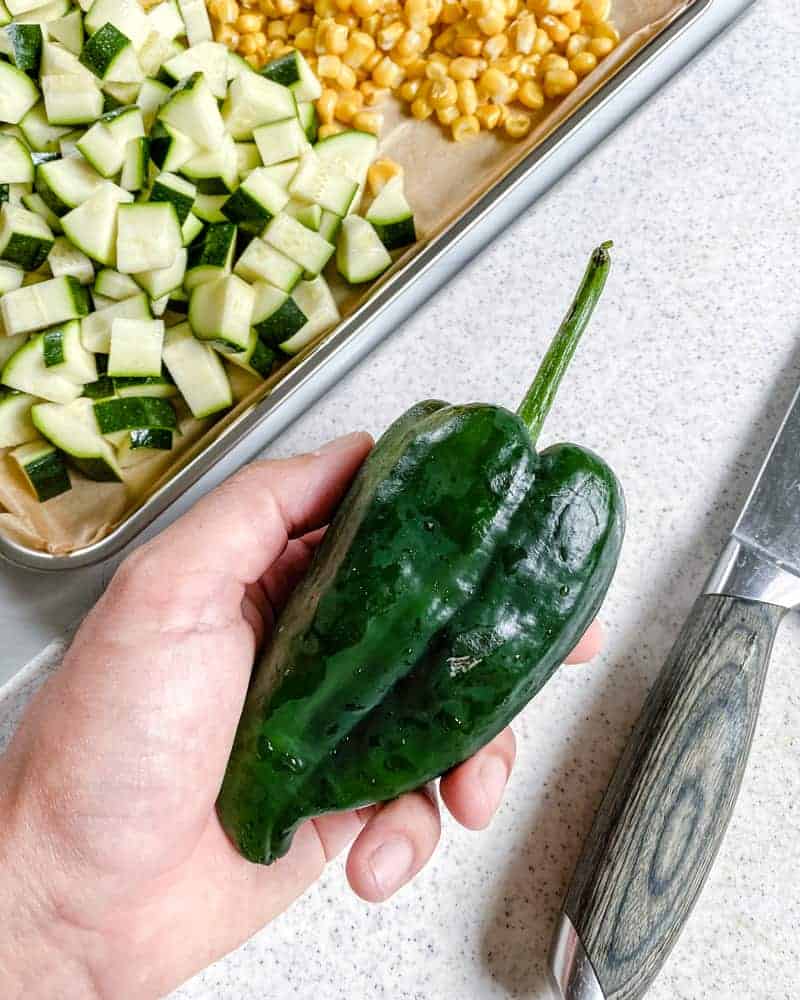 green pepper with knife against a white background with chopped ingredients in the background