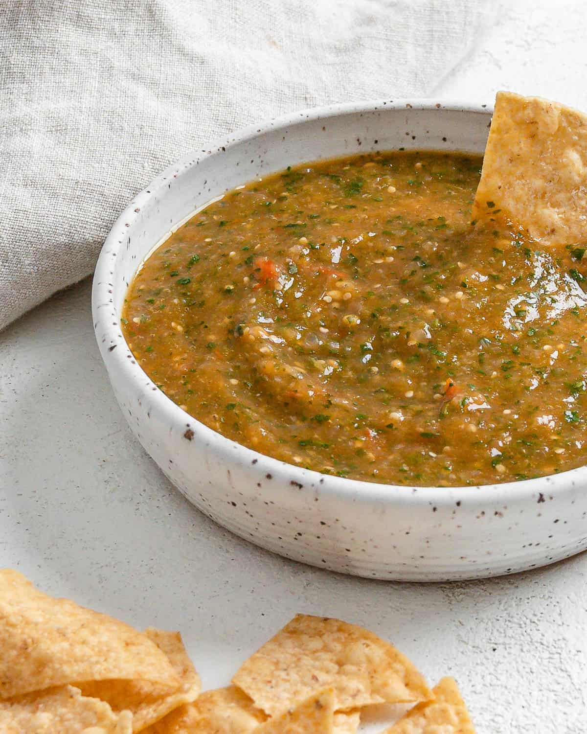 completed Stovetop Tomatillo Salsa in a bowl with a chip being dipped in it