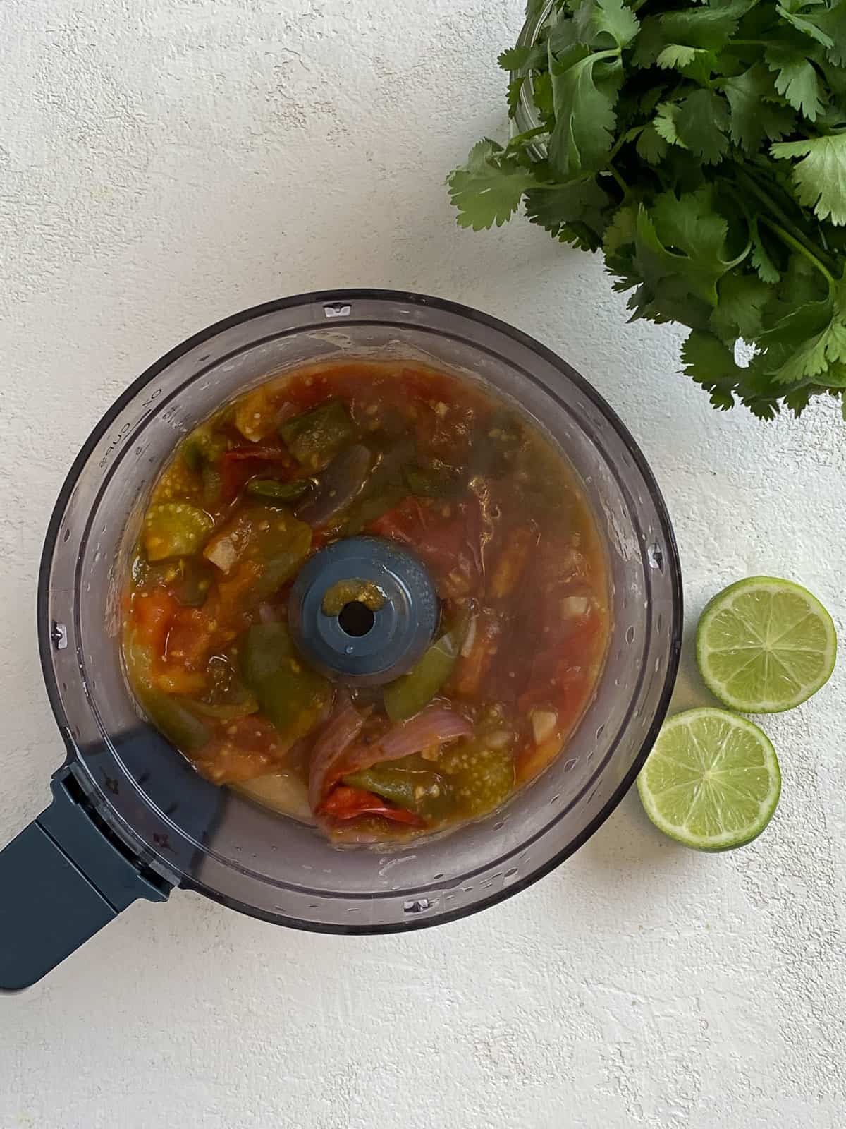 veggies added to food processor against a white background with herbs and lime on the side