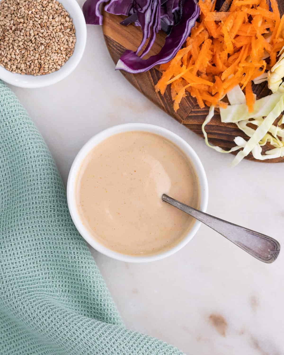 completed slaw dressing in a white bowl with a utensil in it along with veggies in the background