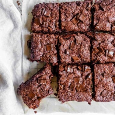 completed vegan Super Fudgy Brownies with a piece cut out on parchment paper