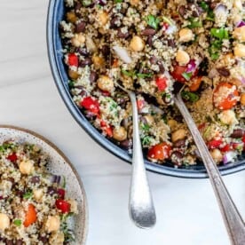 completed Fresh Quinoa Salad in a blue bowl with utensils against a white background