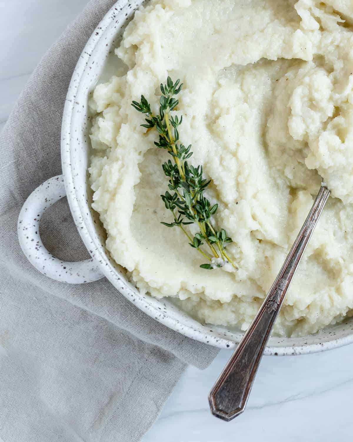 completed mashed cauliflower in a white dish with a spoon in the mashed cauliflower against white background