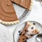 completed Chocolate Pumpkin Pie against a white surface with a slice missing and plated in the background