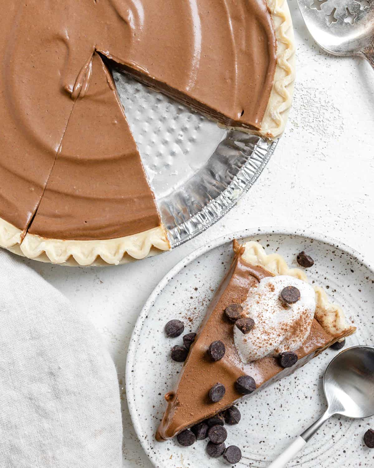 completed Chocolate Pumpkin Pie against a white surface with a slice missing and plated in the background