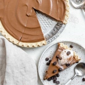 completed Chocolate Pumpkin Pie against a white surface with a slice missing and plated in the background