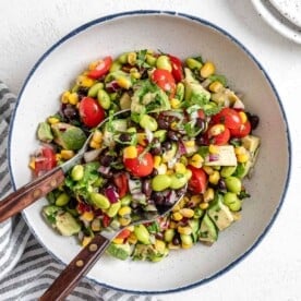 completed white bowl of Easy Edamame Salad with utensils in bowl against a white background