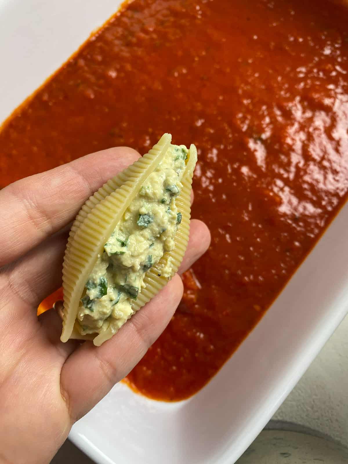 pre-baked stuffed shell being added to baking dish of marinara sauce