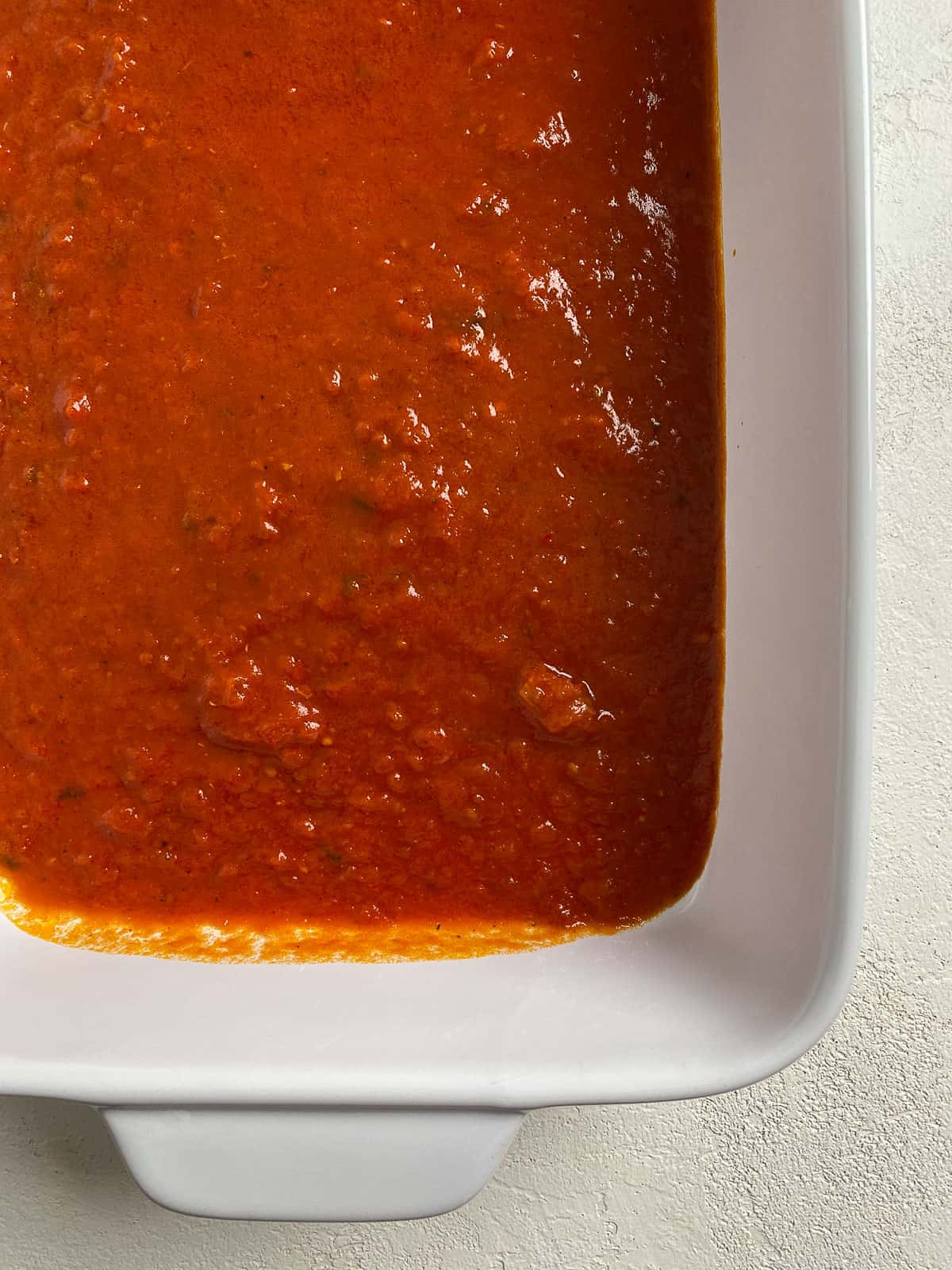 process of marinara sauce being added to white baking dish