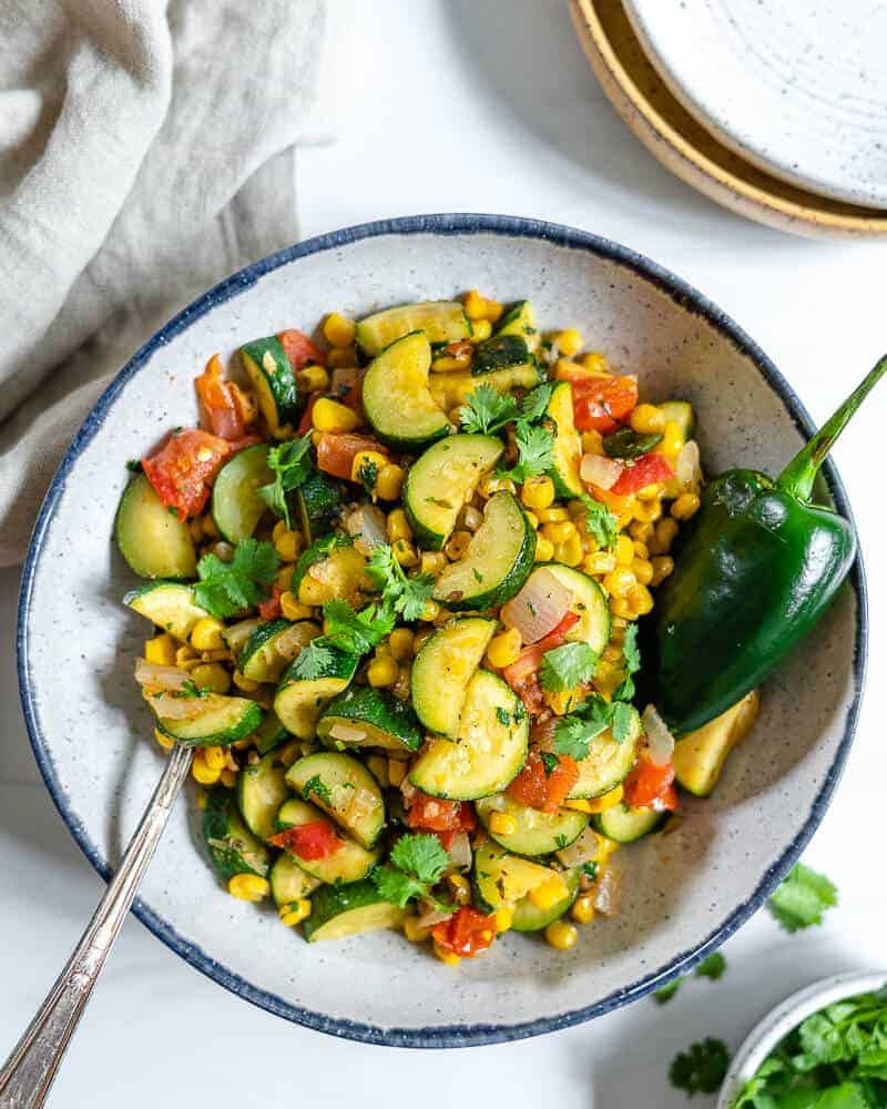 calabasitas recipe with a mixture of veggies in a white bowl with blue rim in a white background