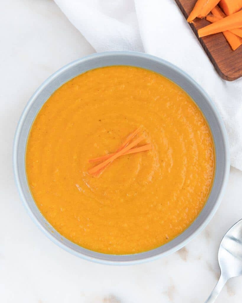 spicy carrot soup in blue bowl against white background with cutting board in the background