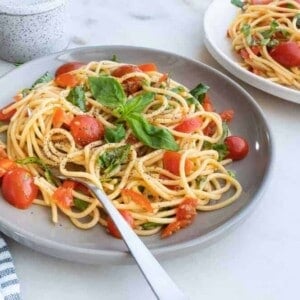 finished plate of Simple Pasta with Tomatoes and Basil on a gray plate on top of a white surface