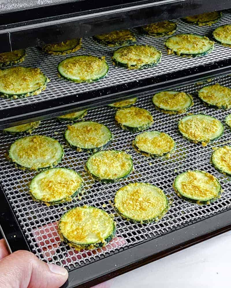 uncooked cheesy zucchini chips on two layered rack