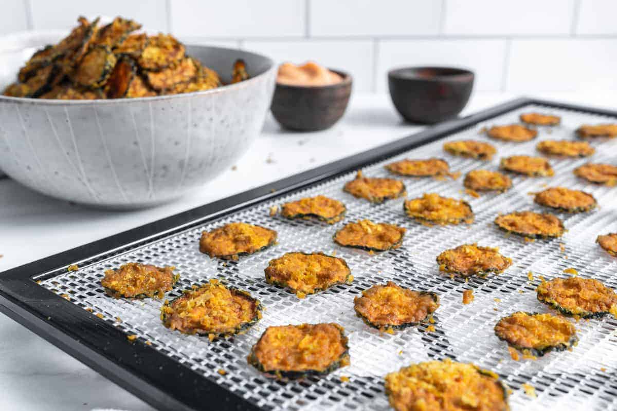 cooked cheesy zucchini chips on rack with a bowl or chips in the background