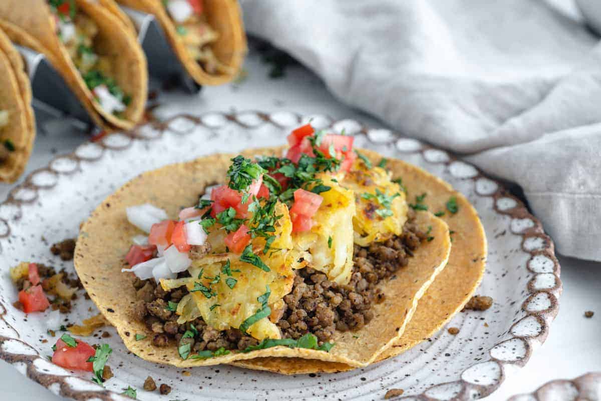 Breakfast Tacos in a white plate with tacos and ingredients in the background against white surface