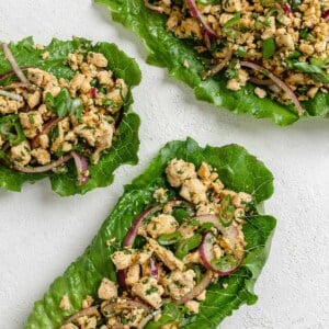 three completed larb salad servings against a white surface