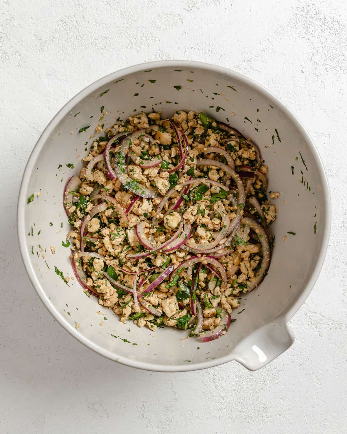 post mixing of larb salad ingredients in a white bowl against a white background