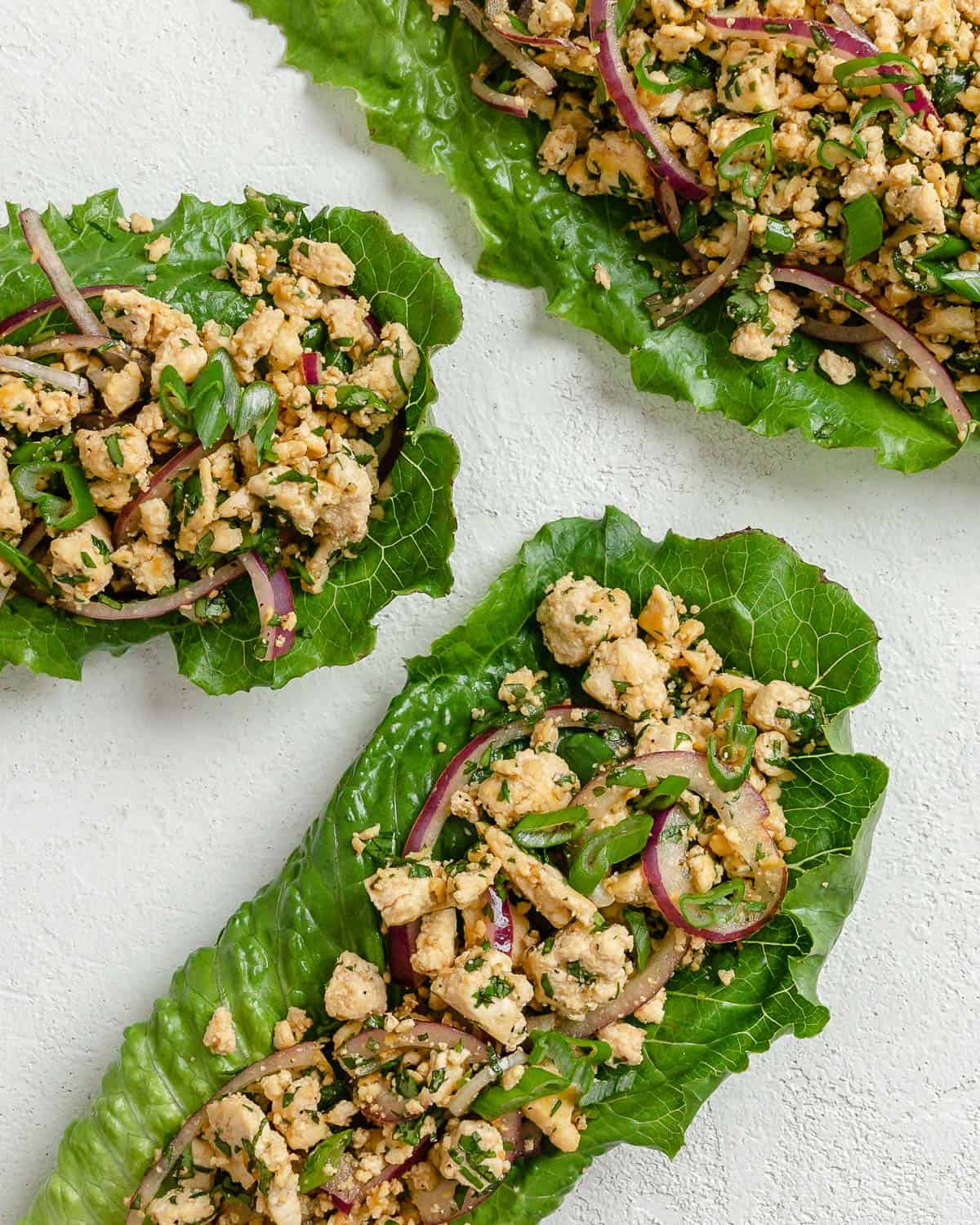 three completed larb salad servings against a white surface