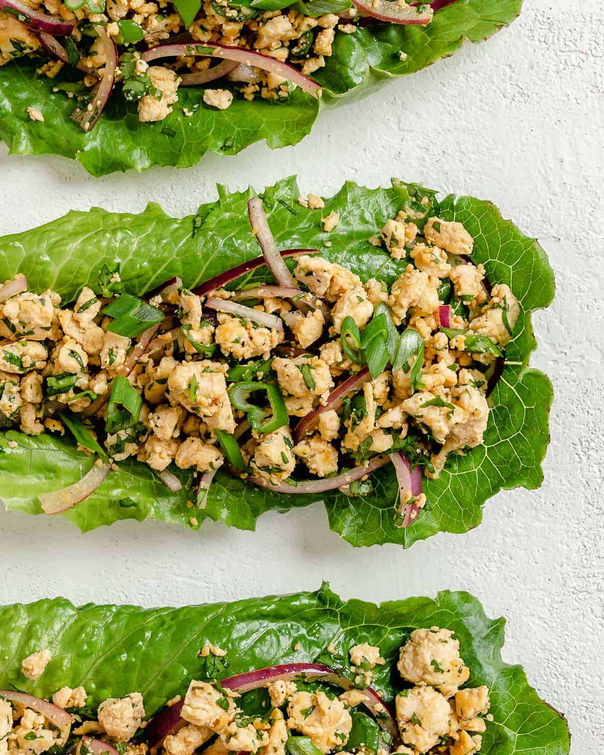 three completed larb salad servings against a white surface