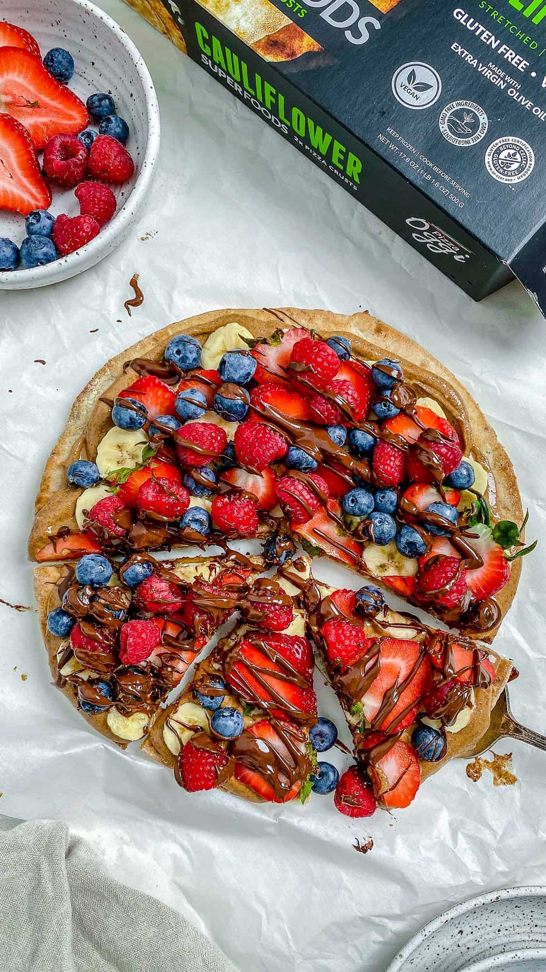 completed fruit pizza with one slice slightly shifted against a white background