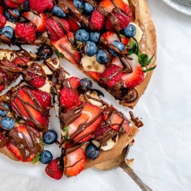 completed fruit pizza with one slice slightly shifted against a white background