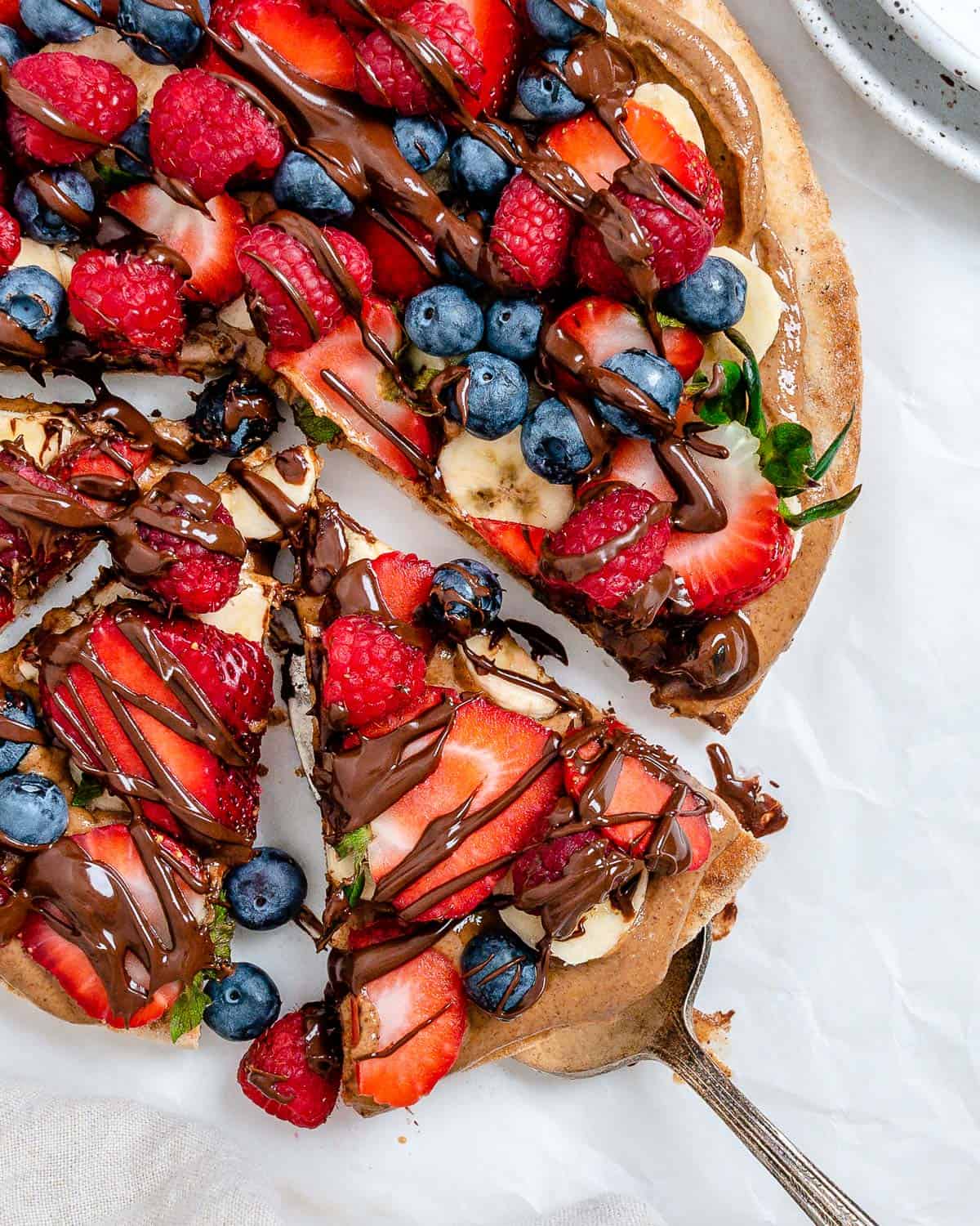 completed fruit pizza with one slice slightly shifted against a white background