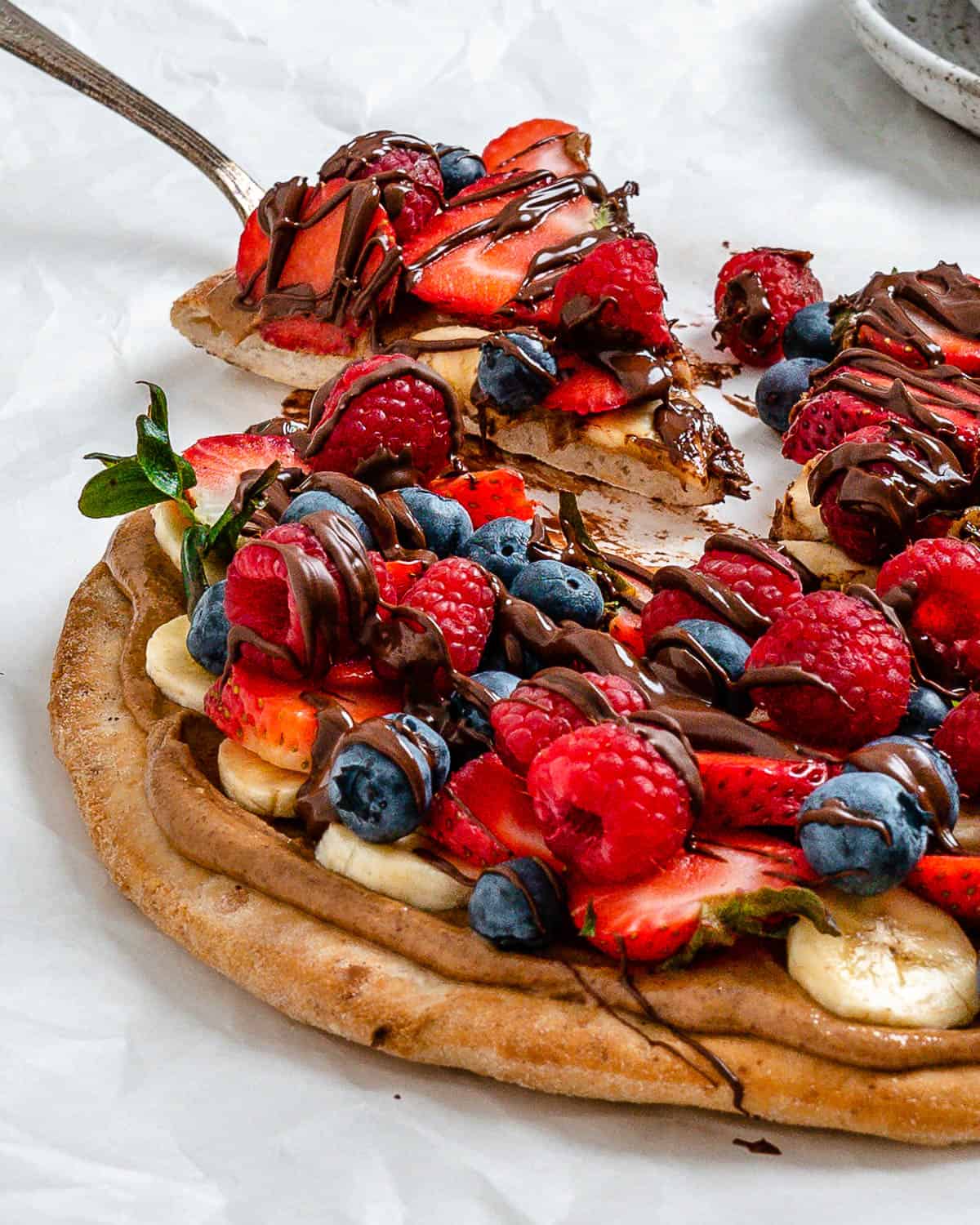 completed fruit pizza with one slice slightly shifted against a white background