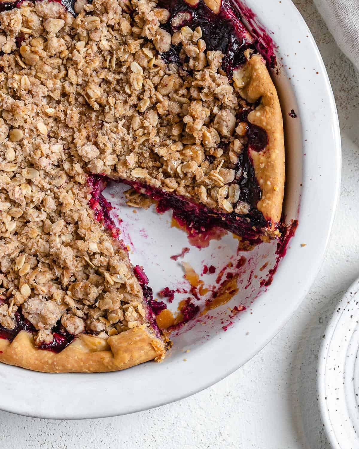 completed Mixed Berry Crumb Pie with a piece plated on a small white plate