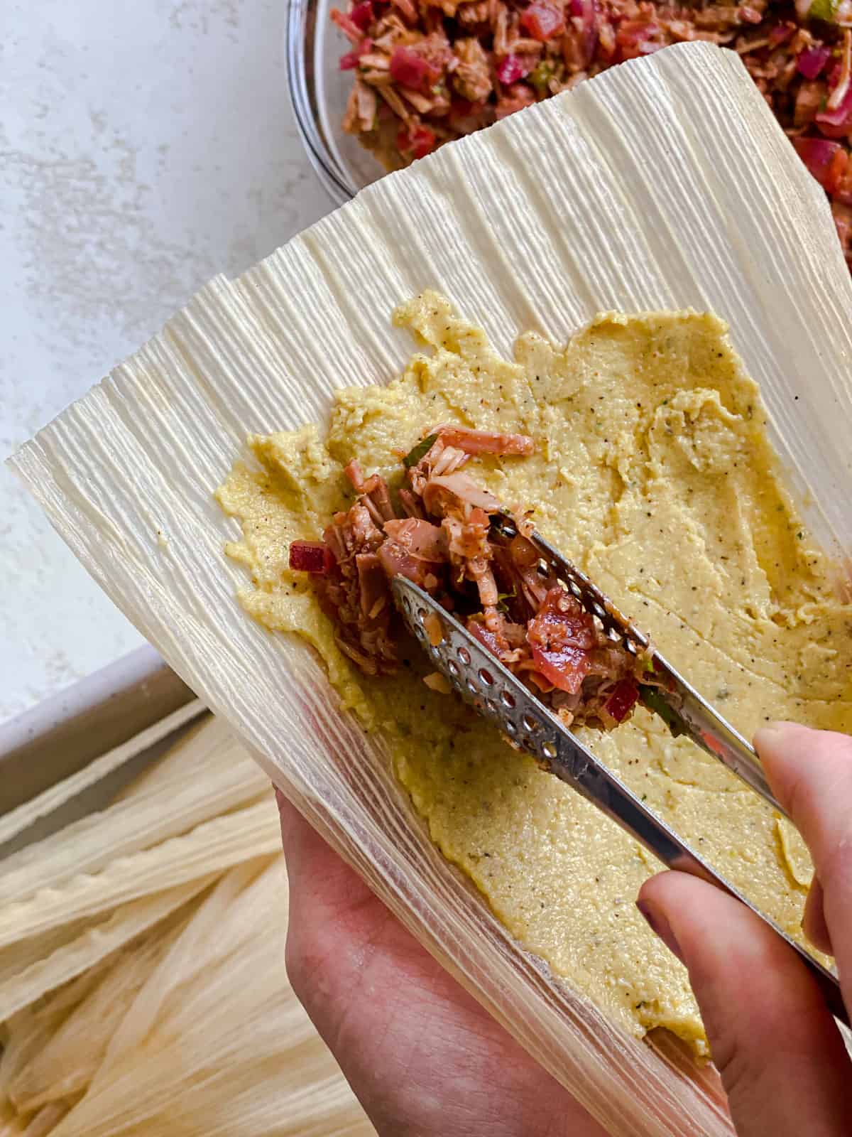 process shot of spreading tamales filling mixture into corn husk