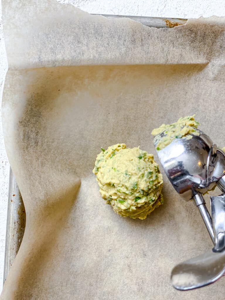 process shot of adding a scoop of baked falafel to baking sheet