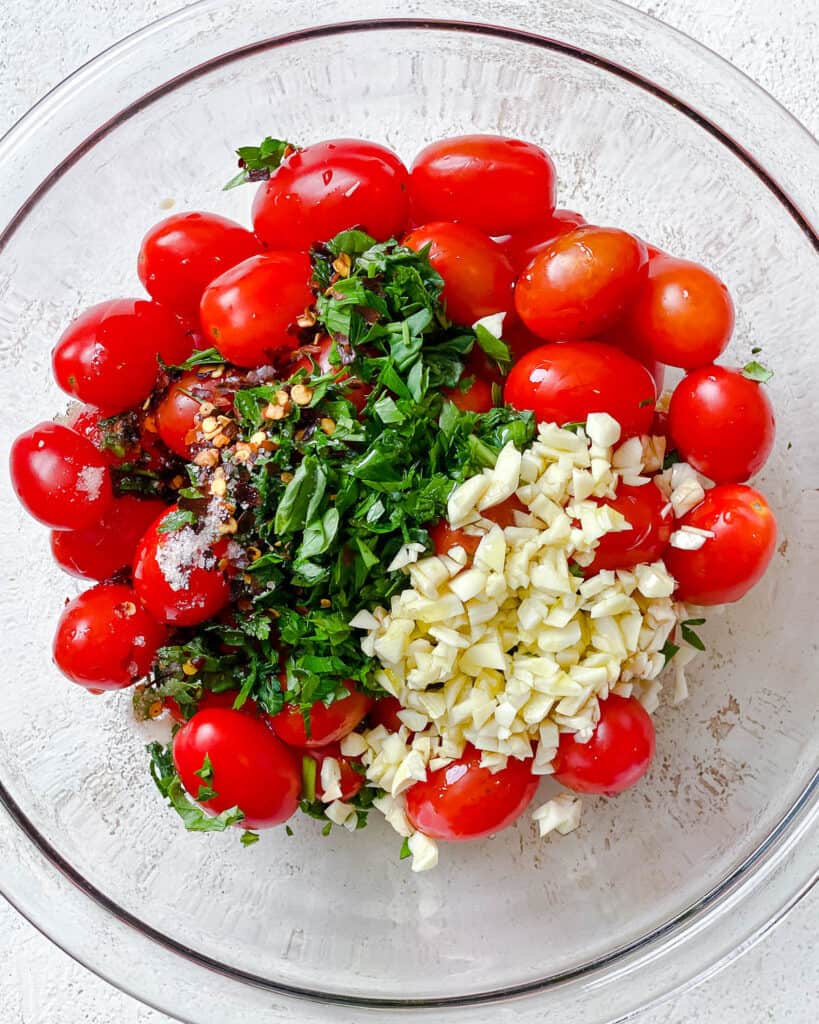 process shot of adding Easy Roasted Cherry Tomatoes ingredients to glass bowl