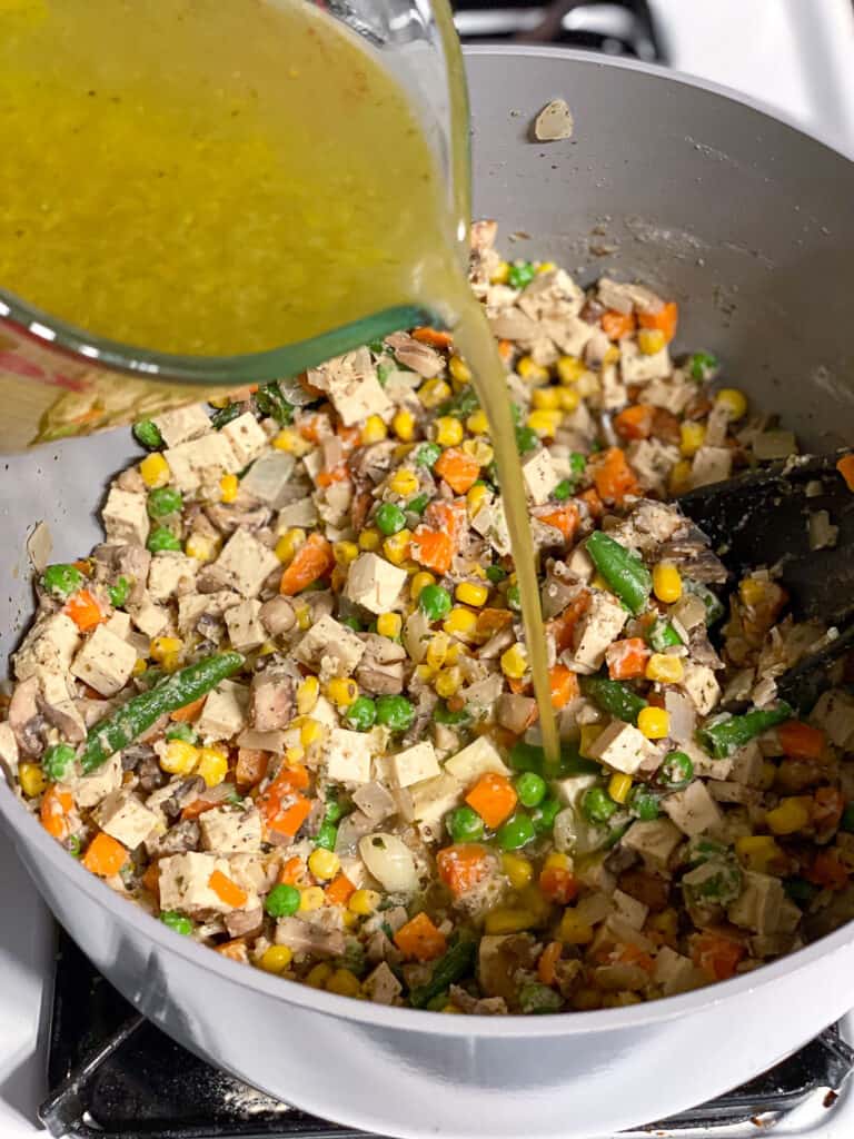 process shot of veggie broth being added to pan