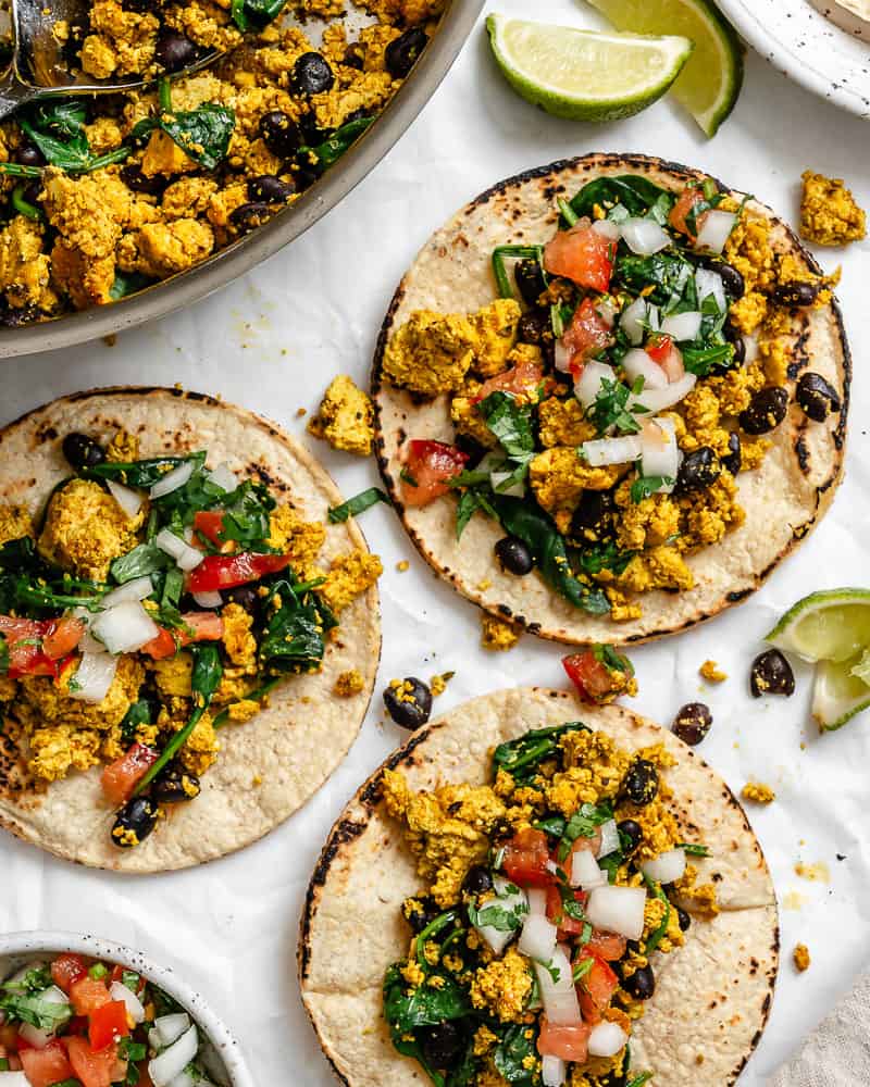 completed Vegan Breakfast Tacos on a white surface alongside pan of filling