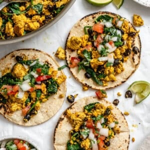 completed Vegan Breakfast Tacos on a white surface alongside pan of filling