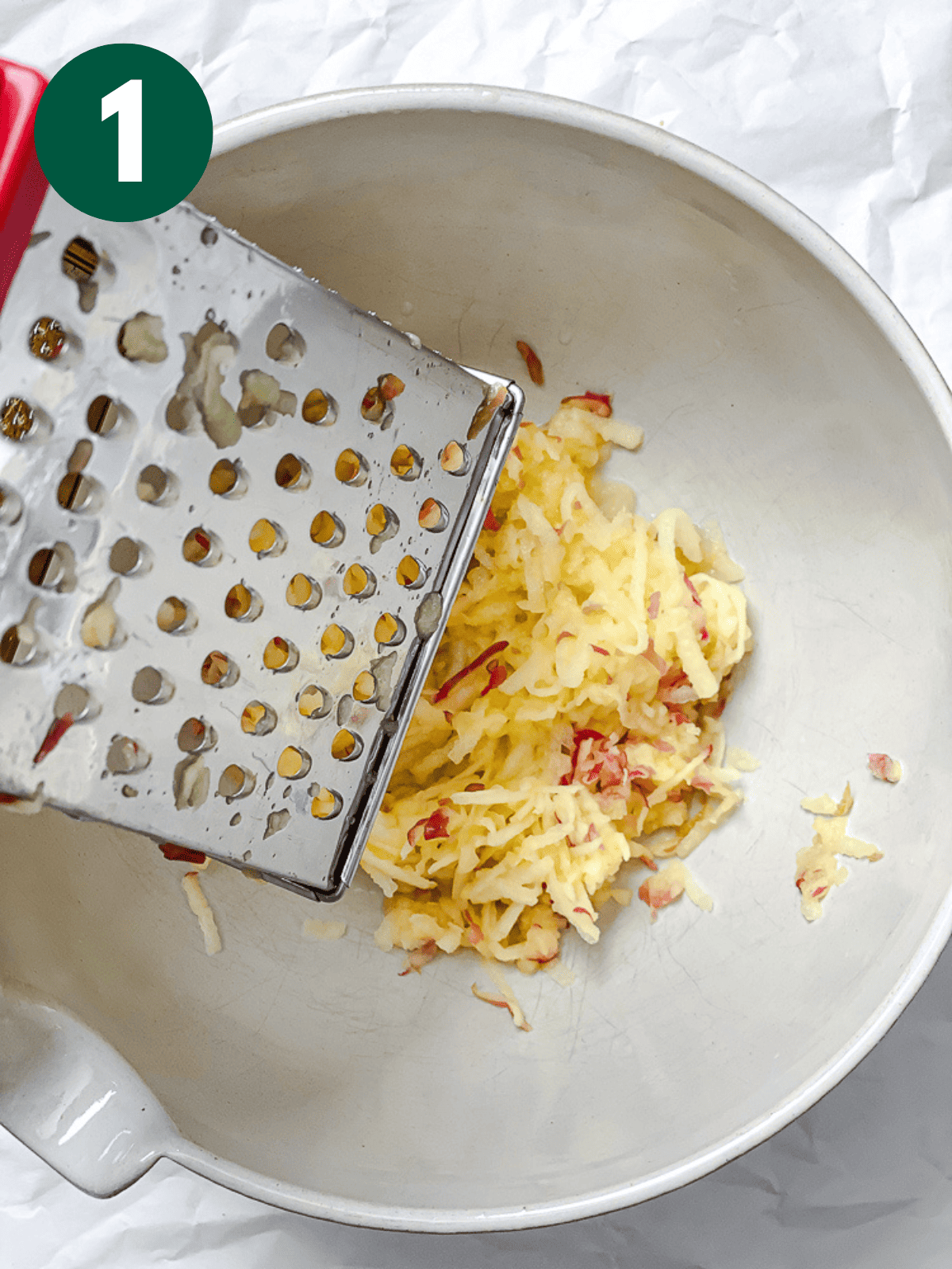 grating apples into a large white bowl.