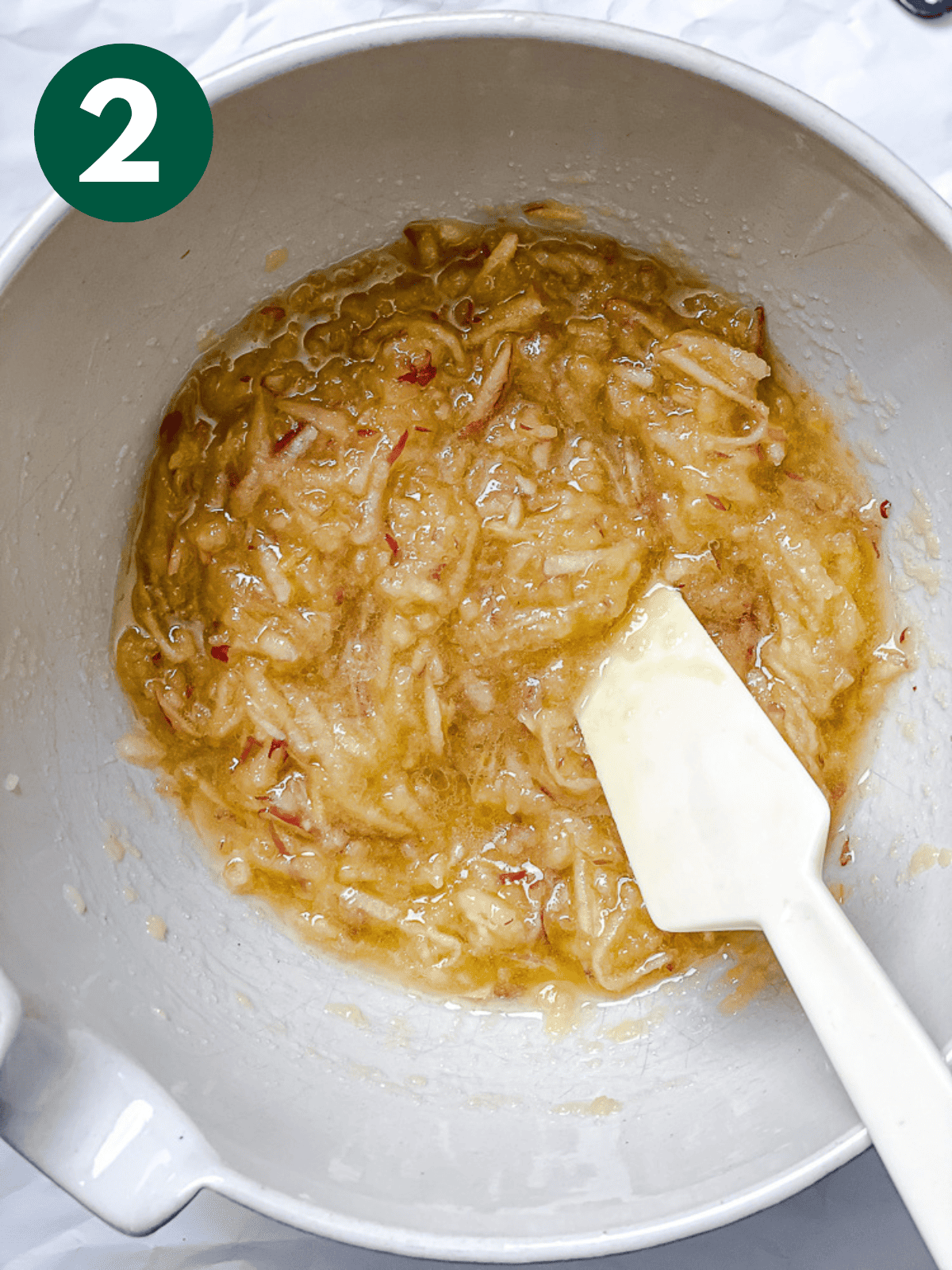 stirring the wet ingredients for apple cinnamon bread with a white spatula in a large white bowl.