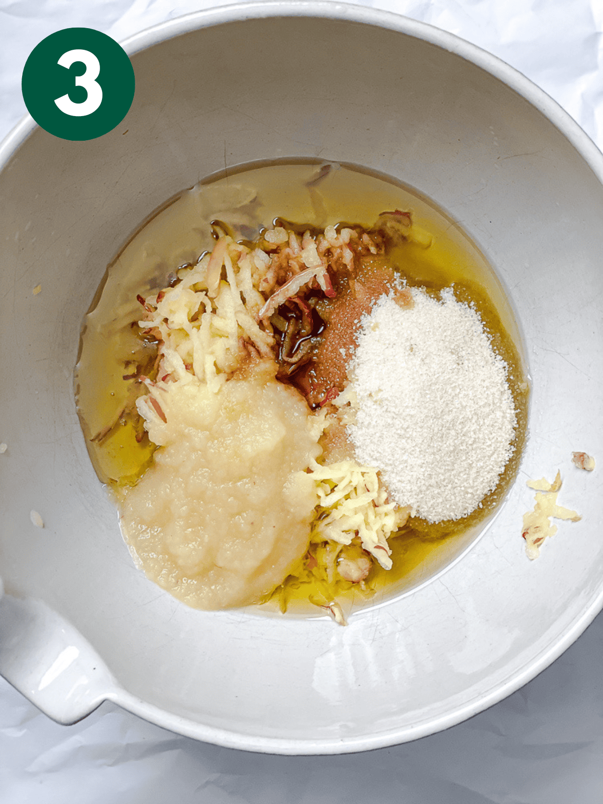 stirring the wet ingredients for apple cinnamon bread with a white spatula in a large white bowl.