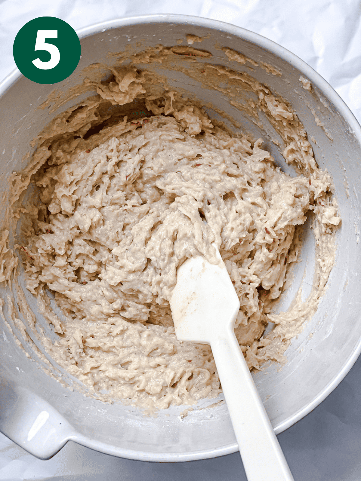 stirring apple cinnamon bread batter in a large white bowl with a white spatula.