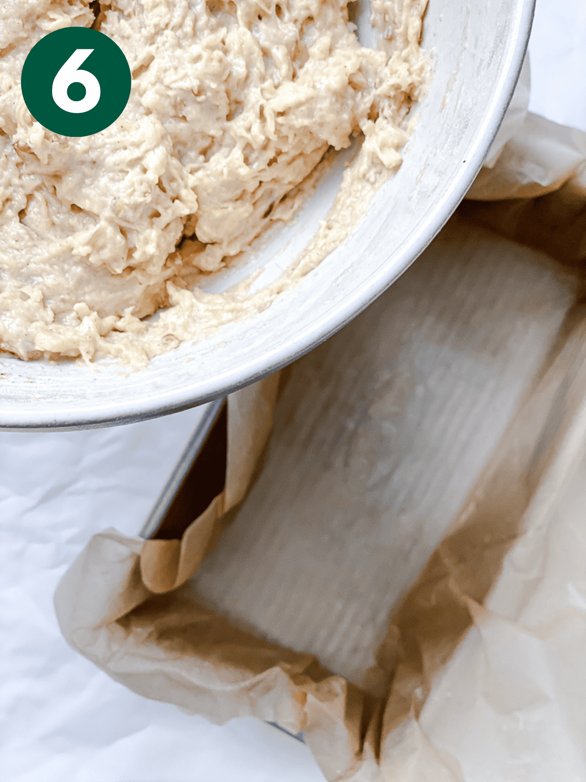 pouring apple cinnamon bread batter into a parchment-lined loaf pan.