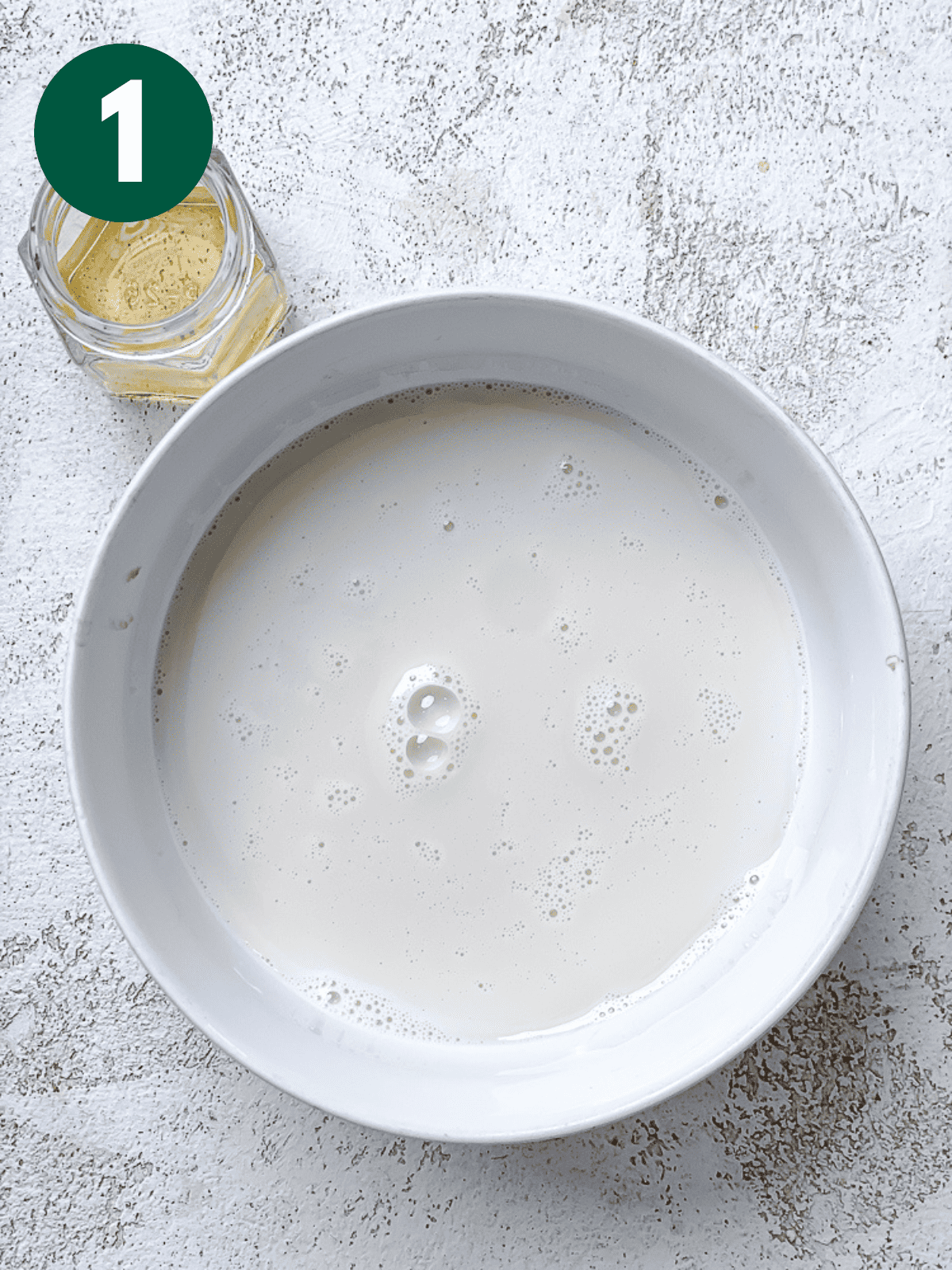 vegan milk in a white bowl next to a small jar of apple cider vinegar.