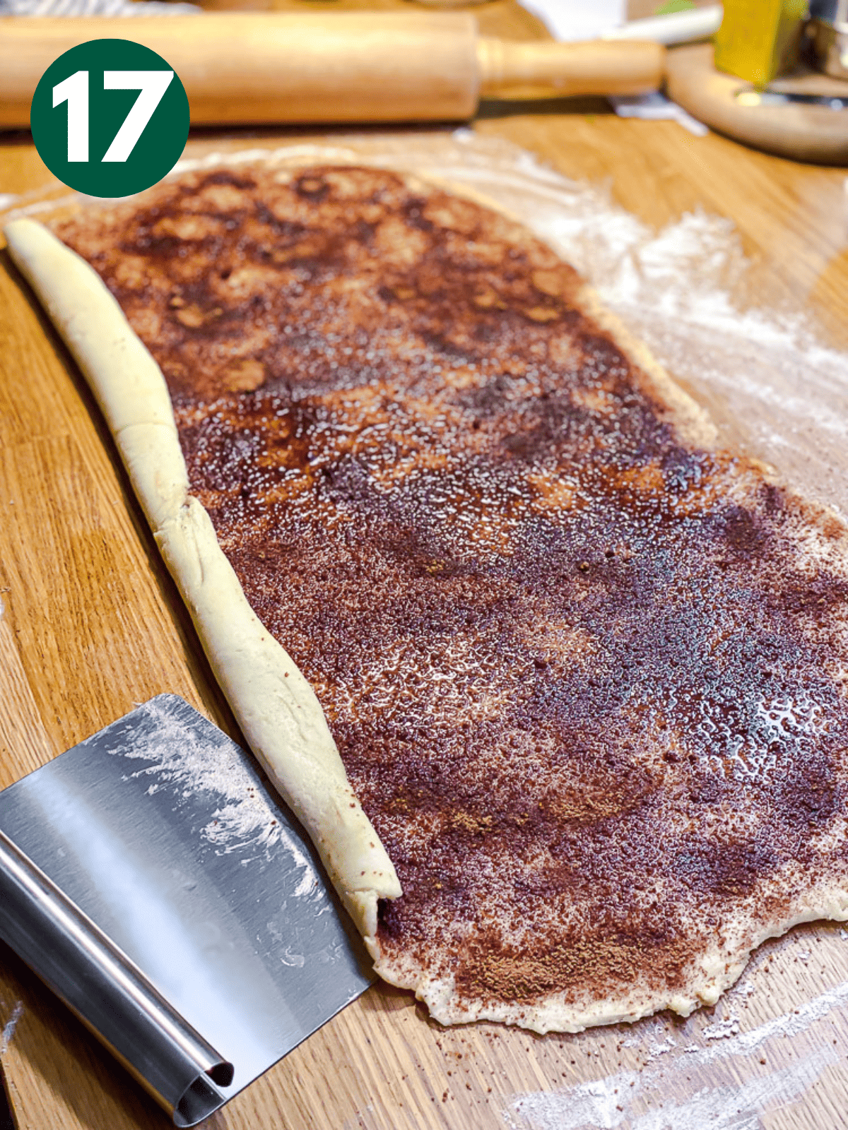 using a metal bench scraper to roll cinnamon roll dough.